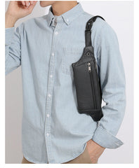 Black leather sling bag worn crossbody over light blue shirt, model front torso view