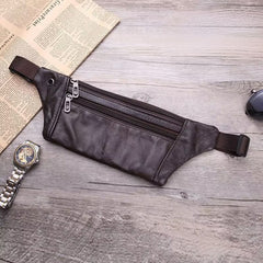 Dark brown leather waist bag flat-lay with newspaper, watch and sunglasses props on wood, top-down view