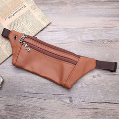 Light brown leather waist bag flat-lay with partial newspaper prop on wood, angled top-down view