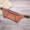 Light brown leather waist bag flat-lay with partial newspaper prop on wood, angled top-down view